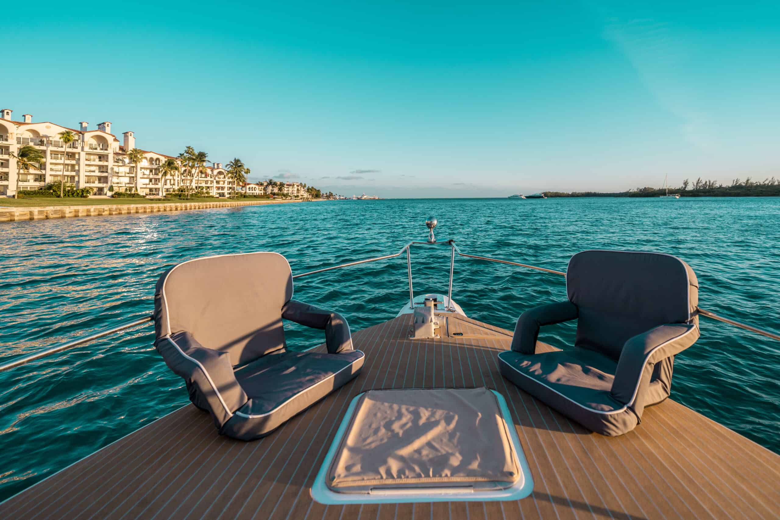 View from the back of a boat in Miami, overlooking calm turquoise waters with coastal buildings in the distance under a clear sky.