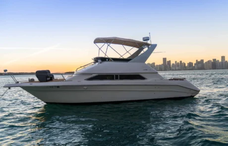 A white boat anchored near the Miami skyline during sunset, with calm blue waters surrounding it.