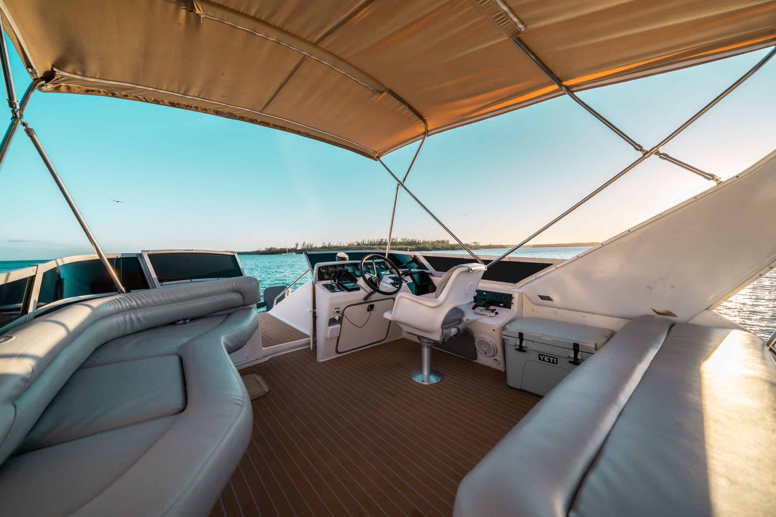 View from the rear of a boat in Miami showing the steering wheel and seating area under a canopy, with a coastal landscape in the background.