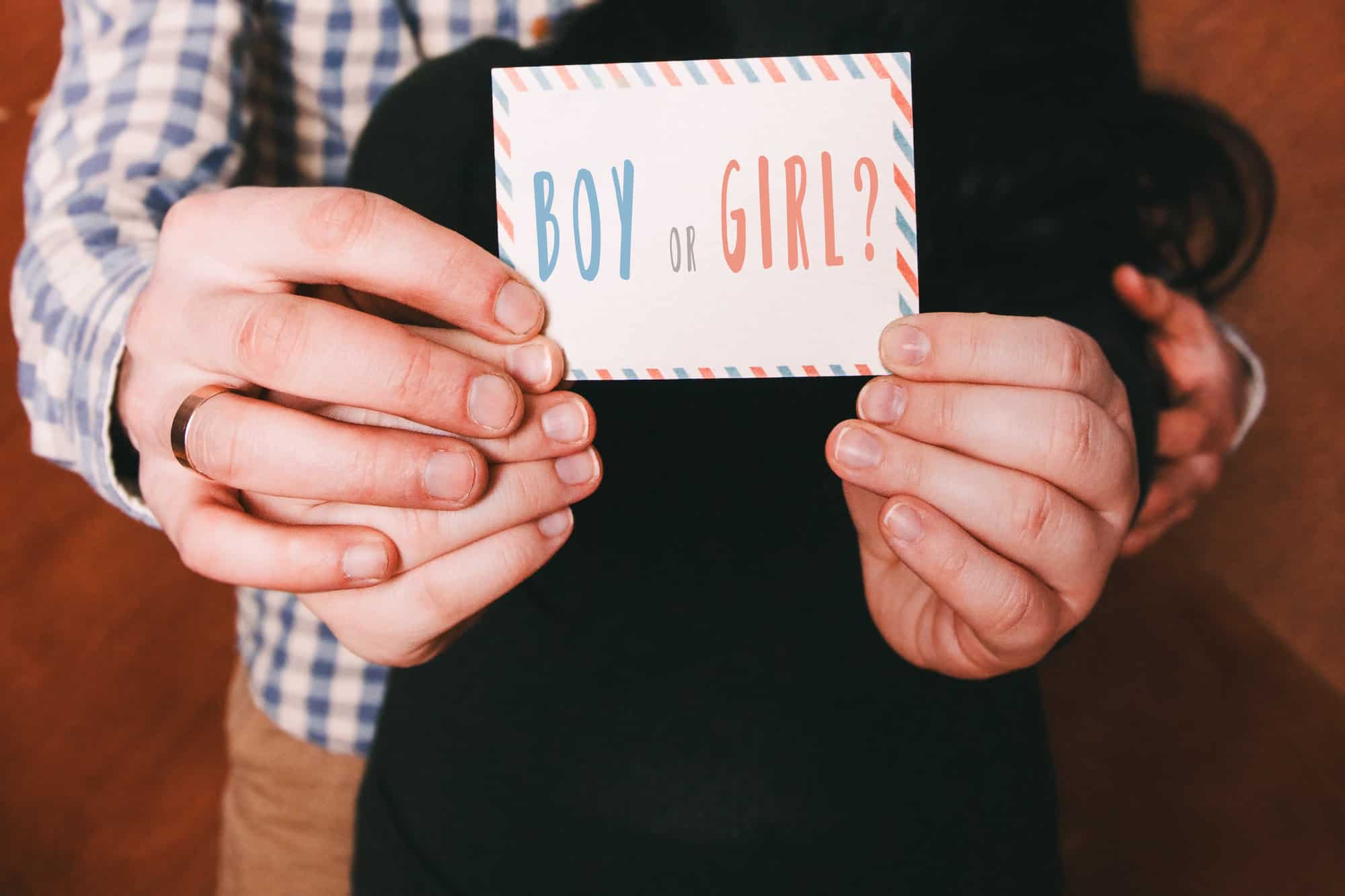 A person holding a card that reads "boy or girl?" with a striped blue and orange border aboard a boat in Miami, indicating a gender reveal event.