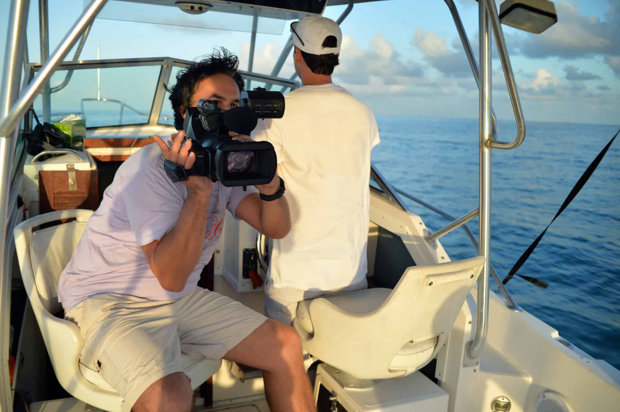 Man filming another man steering a boat on the ocean near Miami at sunset.