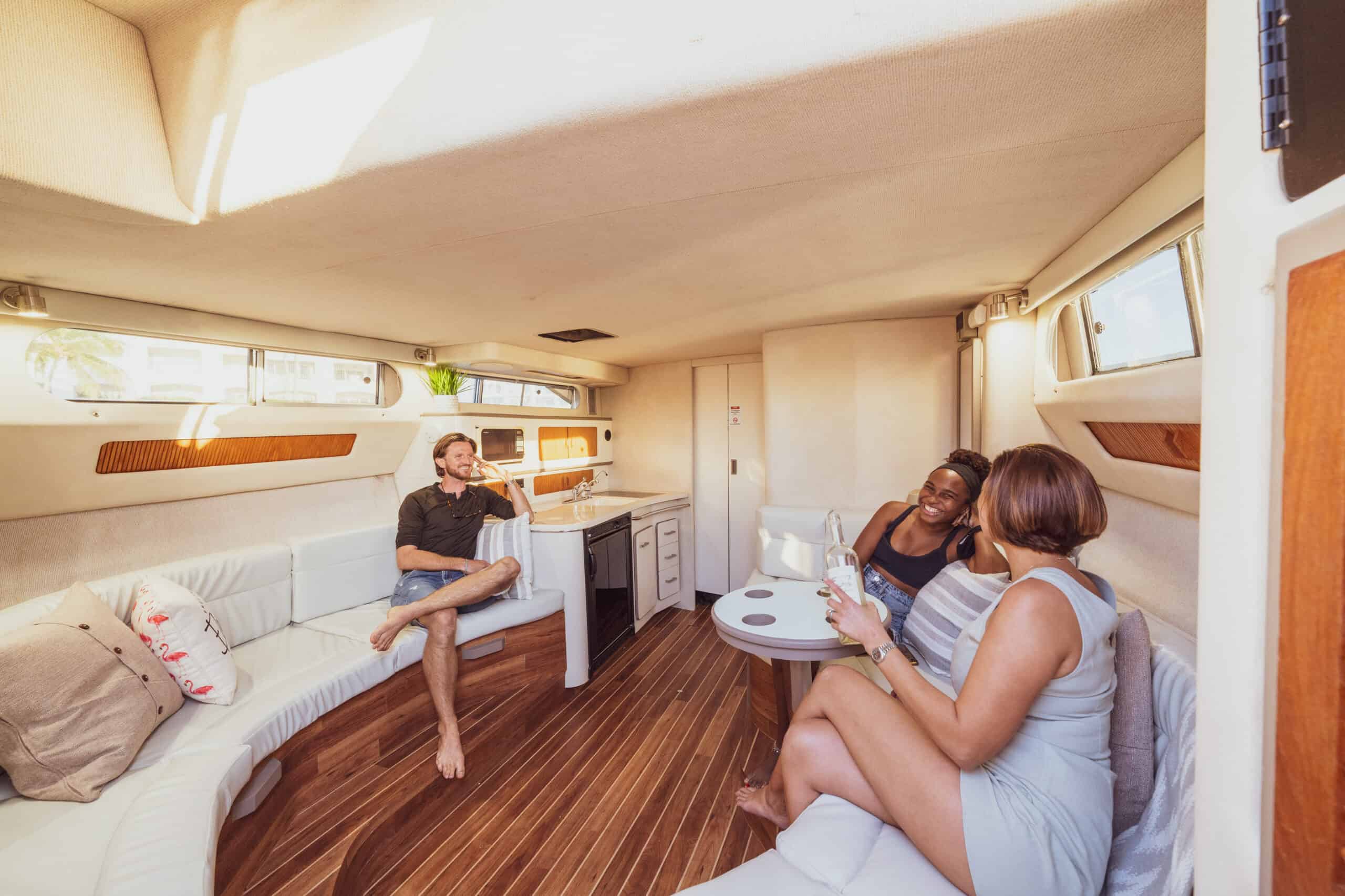 Two women and a man enjoying conversation in a cozy, well-lit boat cabin with modern interior design off the coast of Miami.