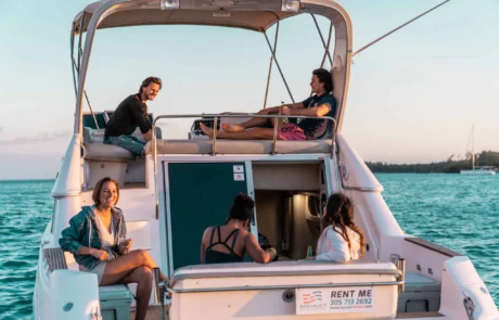 Four people enjoying a sunset boat ride in Miami, two lounging at the stern and two seated below near the cabin, with calm ocean waters in the background.