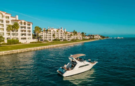 A boat traveling near a coastal residential area in Miami with multi-story white buildings under a clear blue sky.