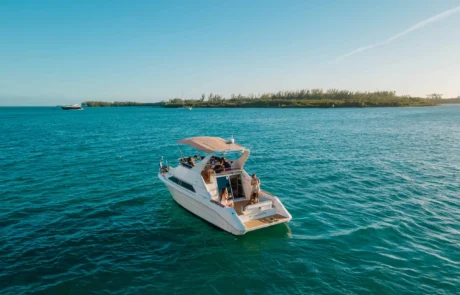 A white luxury yacht with several people on board, anchored in clear blue waters near Miami's coastline under a bright sky.