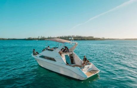 A white boat with several people onboard floating on the blue waters near Miami's shoreline under a clear sky.