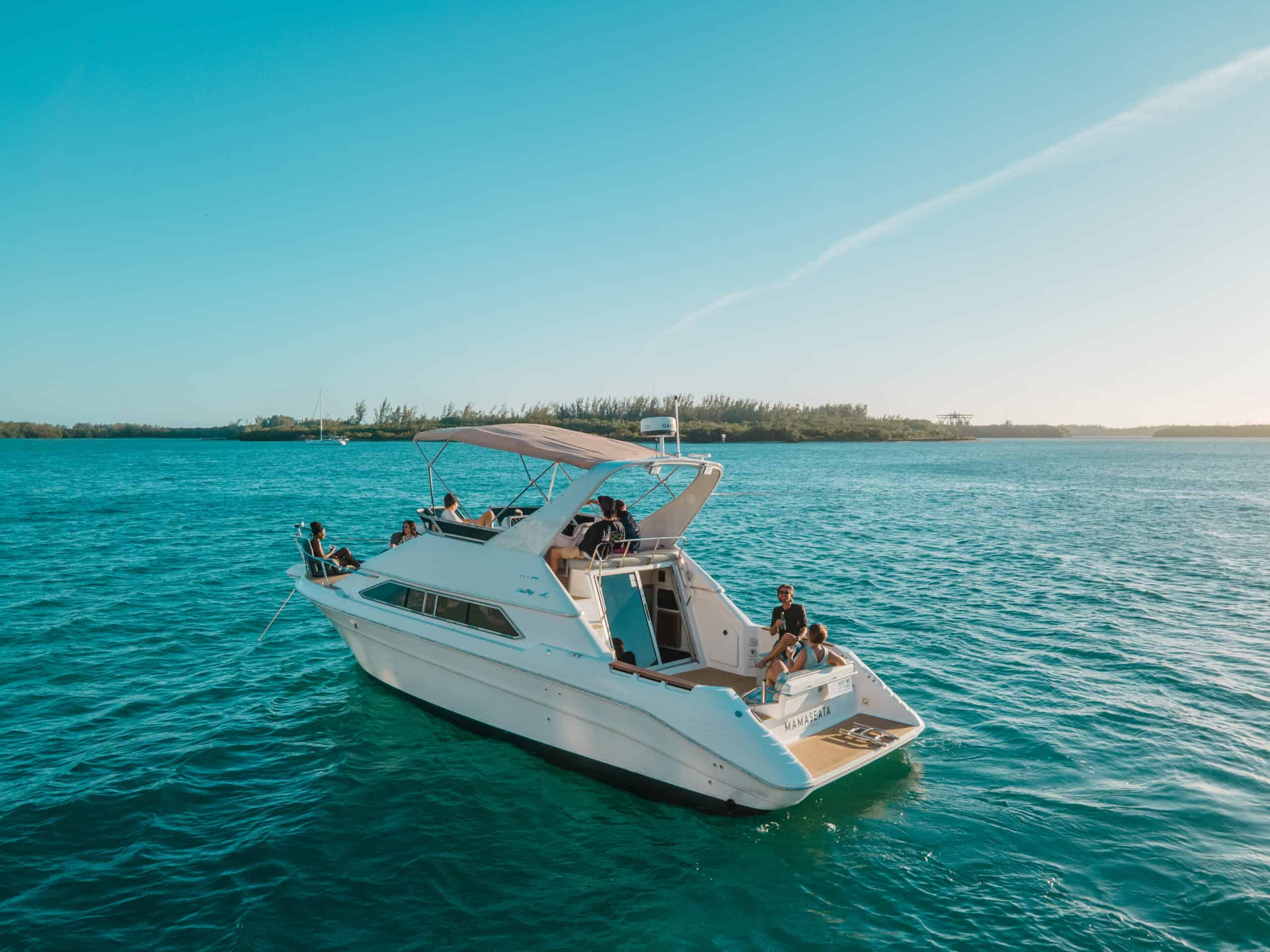 A white boat with several people onboard floating on the blue waters near Miami's shoreline under a clear sky.