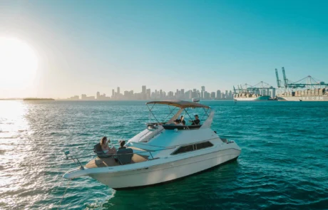 A small boat with two passengers cruising near the Miami skyline and port cranes under a clear blue sky. A small boat with two passengers cruising near the Miami skyline and port cranes under a clear blue sky.