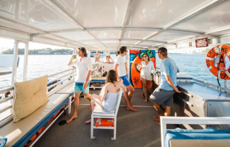 Group of people enjoying a boat ride in Miami on a sunny day, with some standing and others sitting, talking and drinking refreshments.