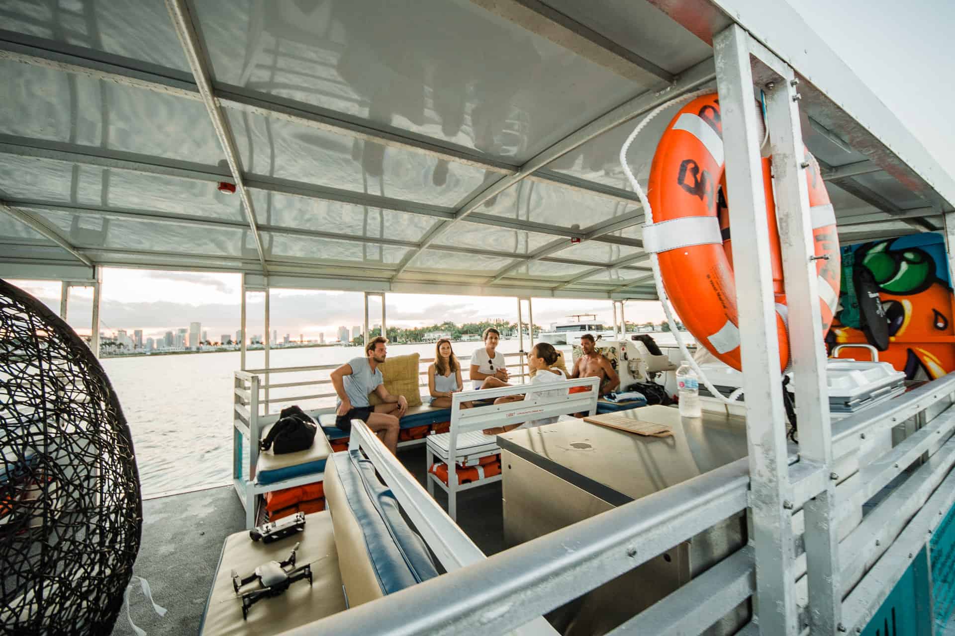 Group of people sitting and talking on a boat in Miami with city skyline in the background during sunset.