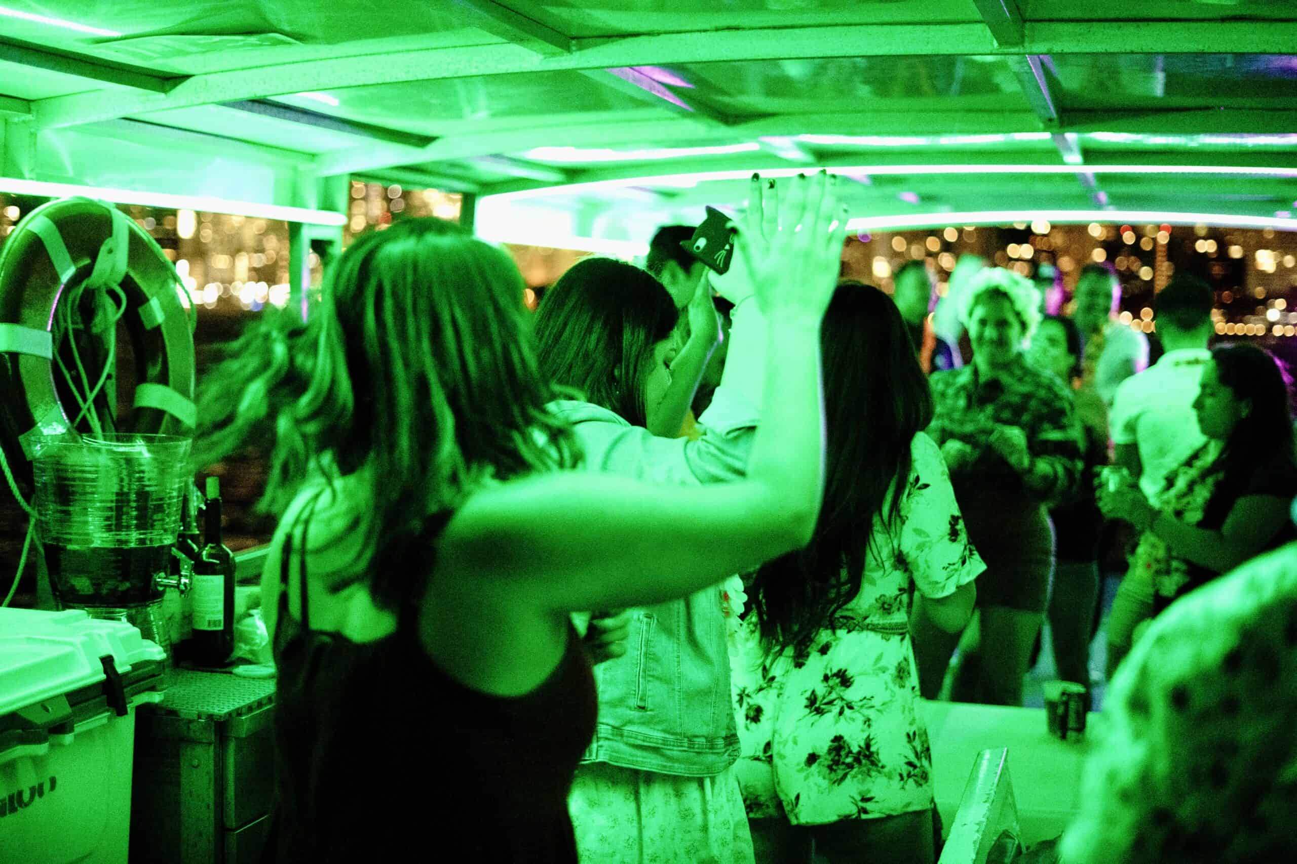 People dancing under green lights on a boat party in Miami at night.