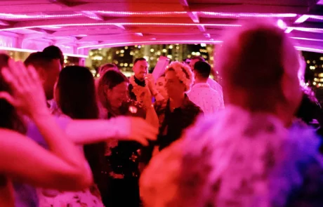 A lively dance floor with people dancing under pink and purple lighting, with focus on a central couple enjoying the moment.