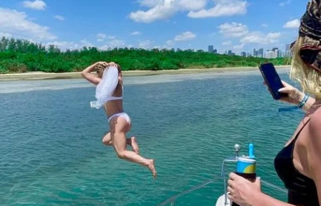 A person jumps off the back of a boat in Miami into a river, with another person watching, under a clear blue sky.