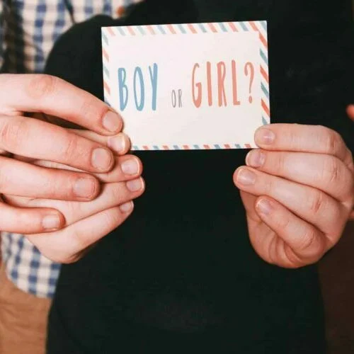 Hands holding a card that reads "boy or girl?" in colorful letters aboard a boat in Miami, suggesting a gender reveal event.