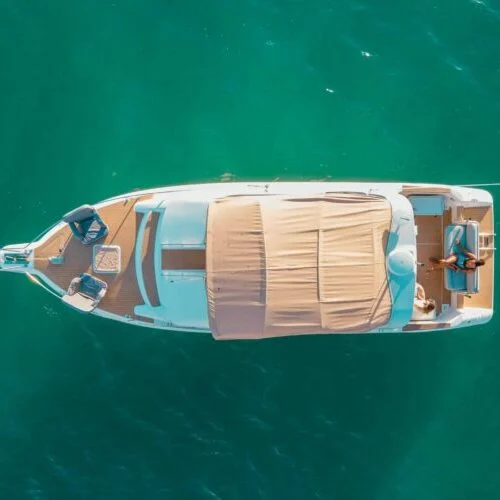Aerial view of a luxury yacht floating on the clear turquoise waters near Miami, featuring a covered deck area and neatly arranged seating.