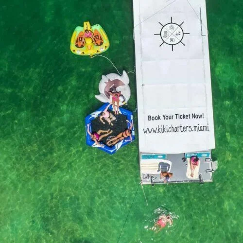 Aerial view of a person on a floating raft next to a boat in Miami advertising boat rides in clear green water.
