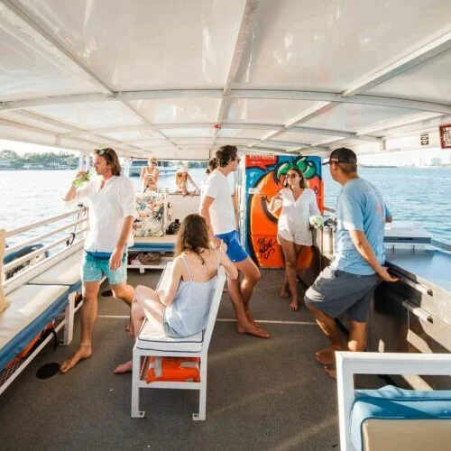 Group of people enjoying drinks and socializing on a boat in Miami with a scenic river backdrop.