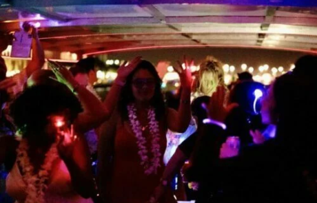 People dancing at a nighttime party on a Miami boat with colorful neon lights.
