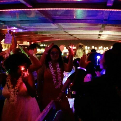 People dancing at a nighttime party on a Miami boat with colorful neon lights.