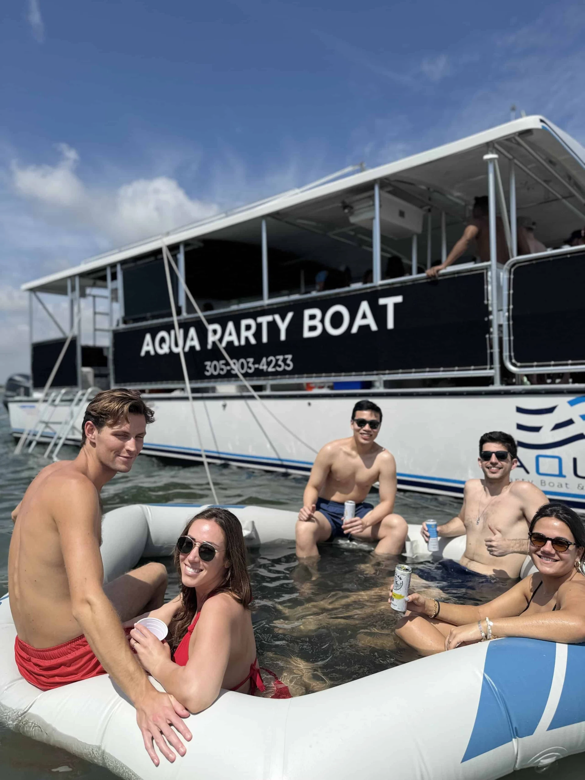 Group of friends enjoying drinks on a floating ring near the “aqua party boat” on a sunny day. Group of friends enjoying drinks on a floating ring near the "aqua party boat" on a sunny day.