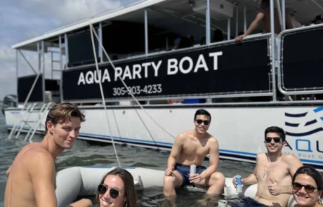 Group of young adults enjoying drinks on an inflatable raft in front of the "Miami aqua party boat.
